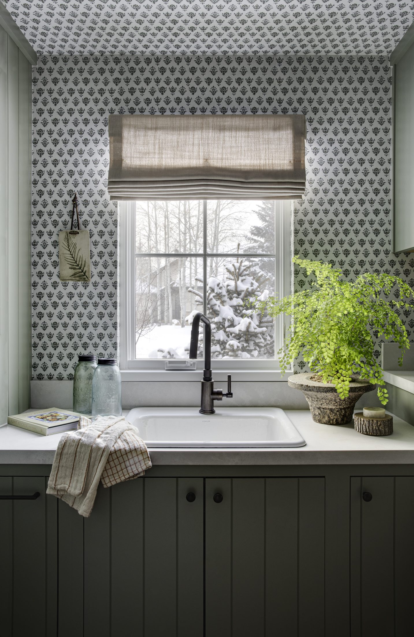 Scullery sink with patterned wallpaper and forest green cabinets