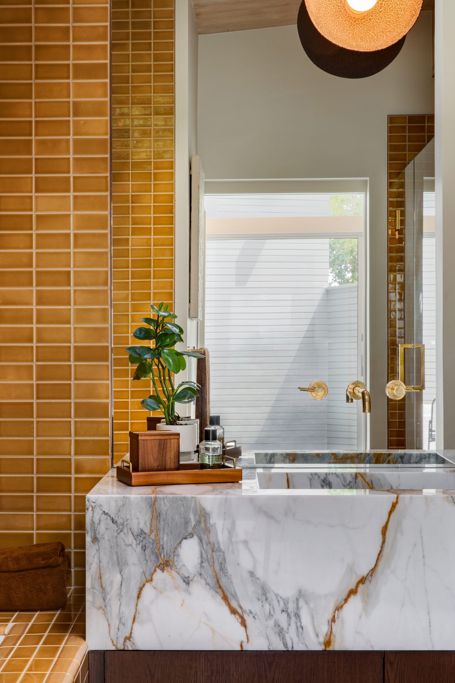 Marble waterfall vanity against a run of glazed ochre tile