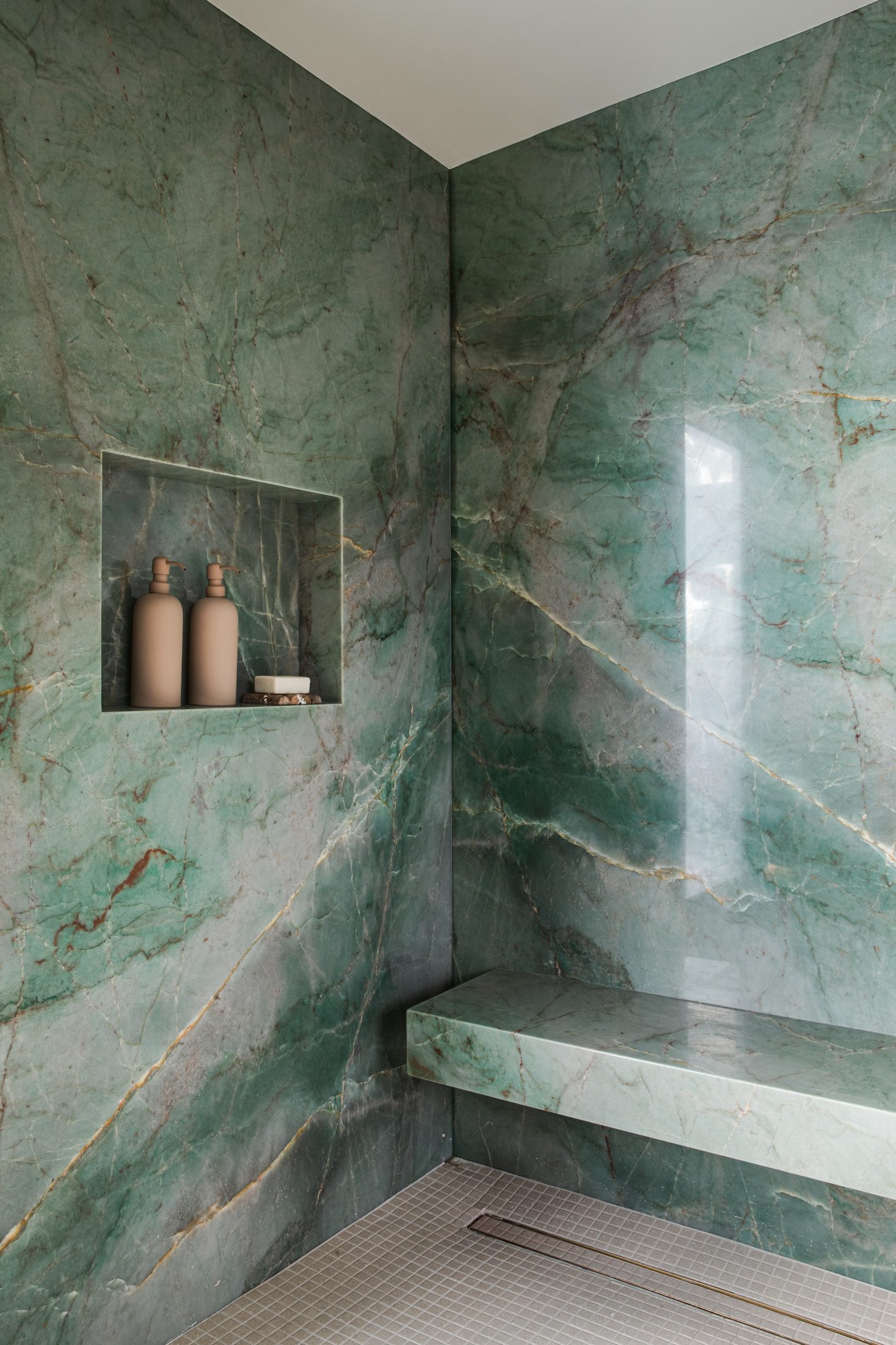Green marble shower bench beneath a recessed niche