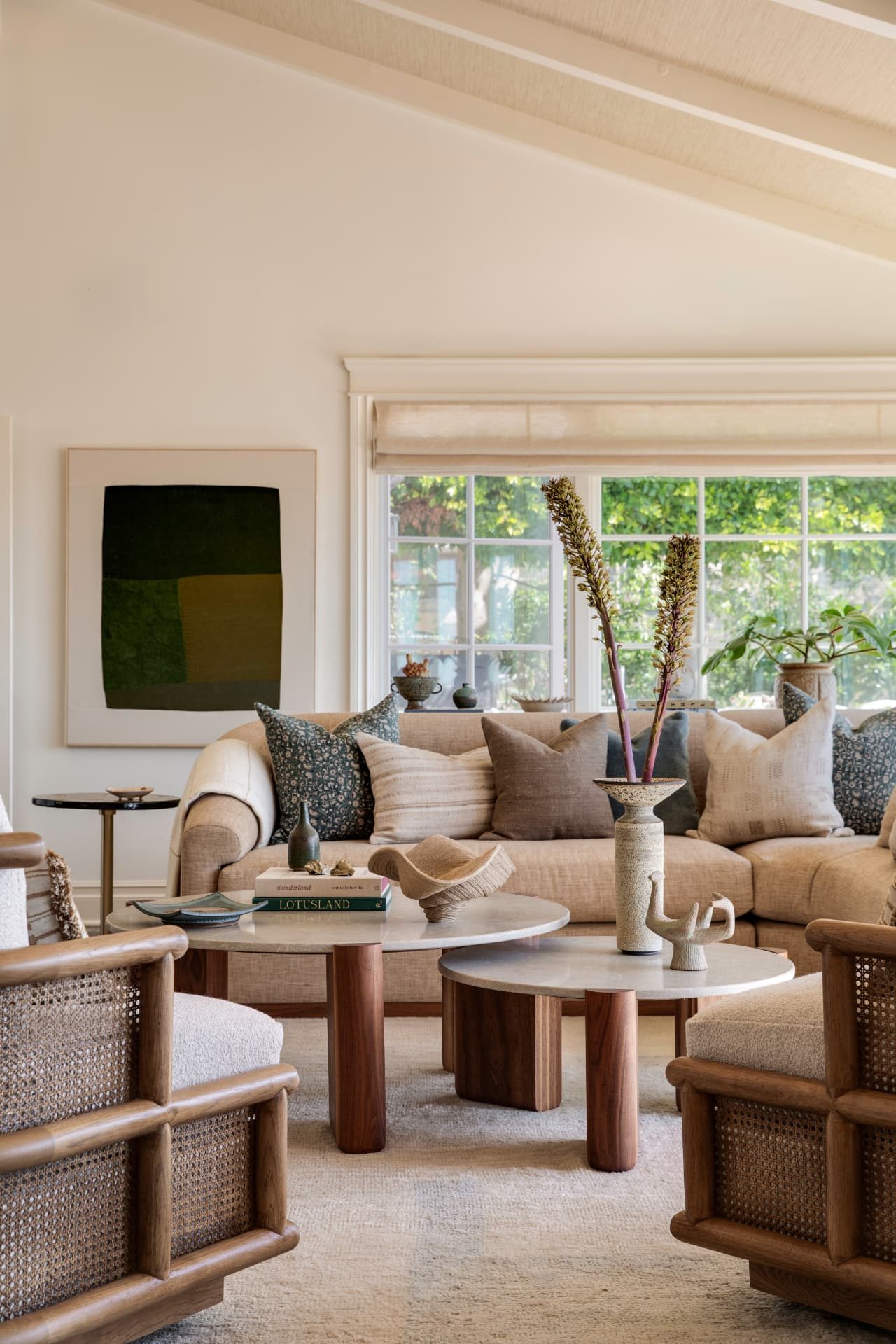 Living room with linen sofa, cane armchairs, and a green textile artwork