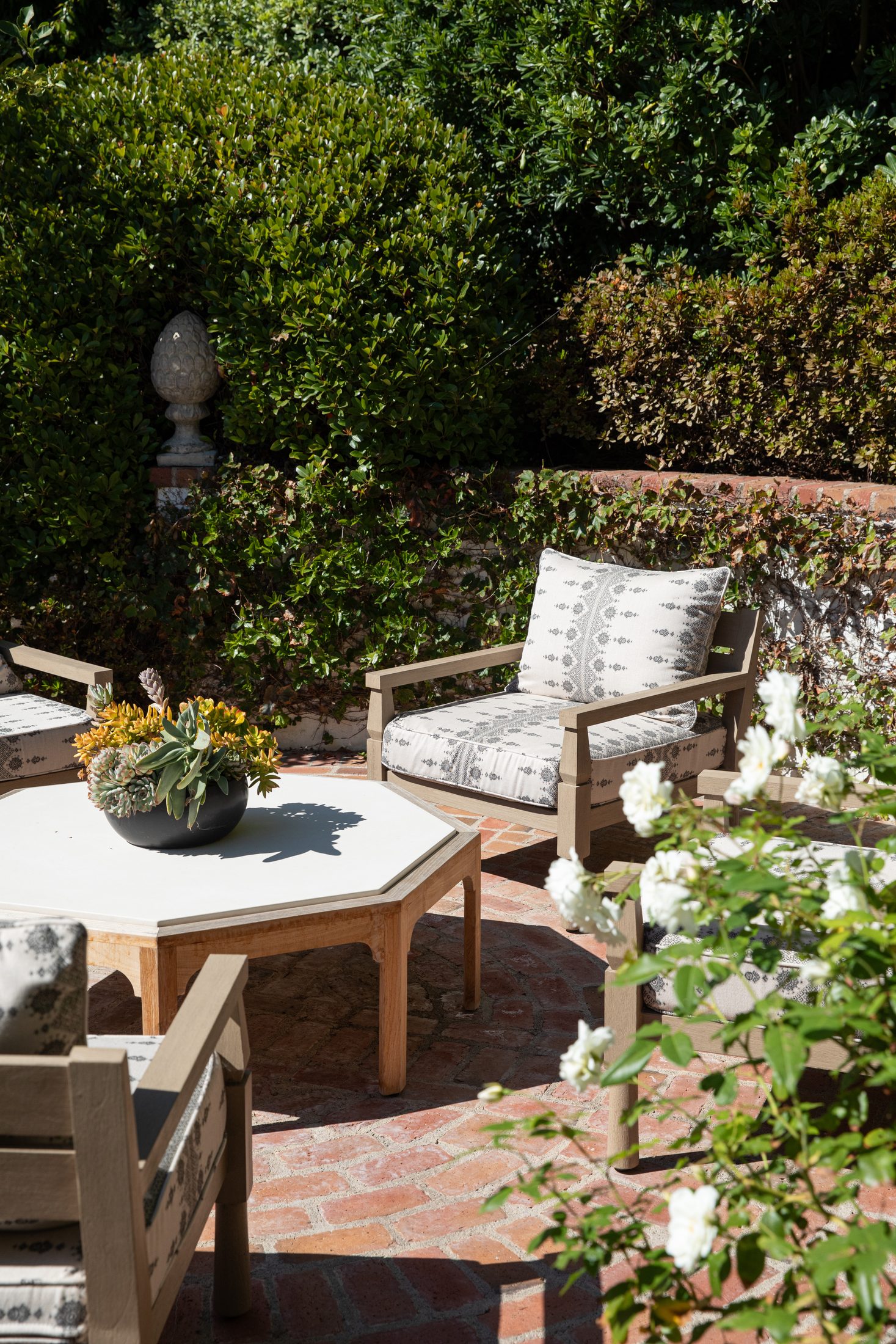 Brick terrace seating area framed by hedges and climbing roses