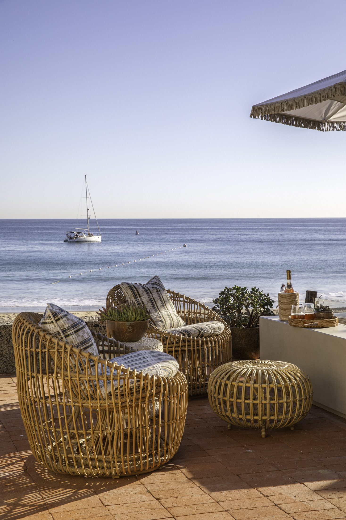Ocean terrace with rattan chairs and a sailboat on the horizon