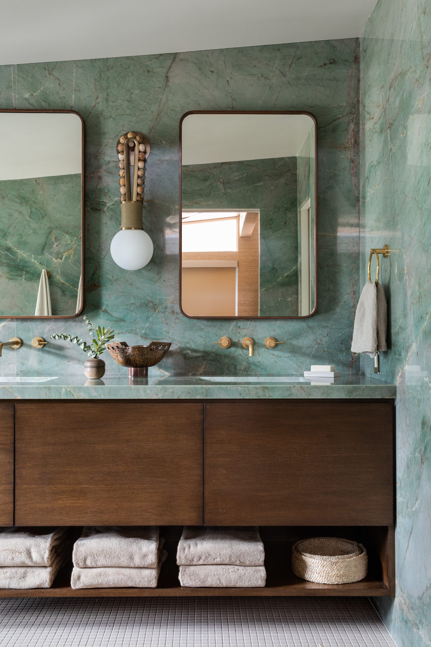 Green marble vanity with rounded mirrors and walnut cabinetry