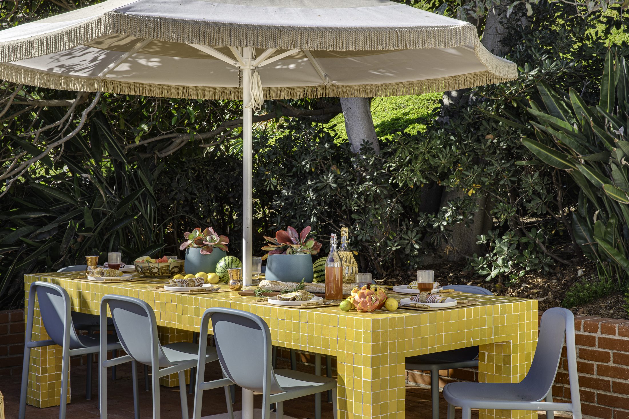 Long dining table in yellow tile beneath a fringed umbrella